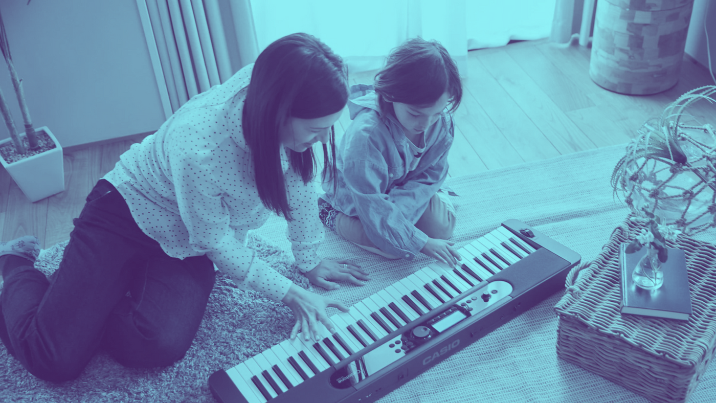 Two people playing a keyboard on the floor in a room.